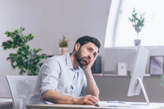 Hombre sentado en su escritorio con la mirada perdida y sujetando su cabeza